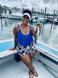 A smiling angler proudly displaying a caught fish while standing on a boat in a marina setting.