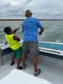 A young angler and an adult are engaged in fishing on a sportfishing boat, showcasing a dynamic fishing experience in a coastal environment.