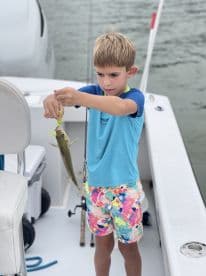 A young angler proudly displaying a caught fish while fishing on a boat, showcasing a fun family fishing experience.