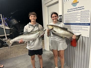 Two young anglers proudly displaying their large Salmon catches at Elmwood Marina after a successful fishing trip.