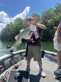 A young angler proudly displaying a large striped bass on a fishing boat, enjoying a sunny day on the water.