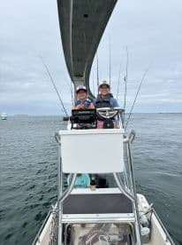 Two young anglers enjoying a fishing trip aboard a center console boat under a bridge, with fishing rods ready for action.