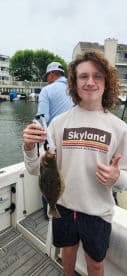 A young angler proudly displaying a Flounder while fishing from a boat, showcasing a fun day on the water.