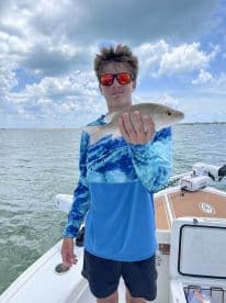 A young angler proudly displaying a caught fish while on a boat, enjoying a day of fishing in a scenic waterway.