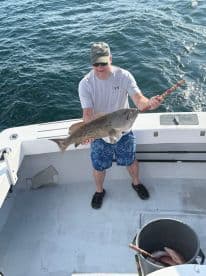 An angler proudly displaying a large Grouper while fishing on a boat, showcasing a successful day on the water.