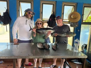 Three anglers proudly displaying their catch of Mahi Mahi and other fish at a cleaning station after a successful fishing trip.