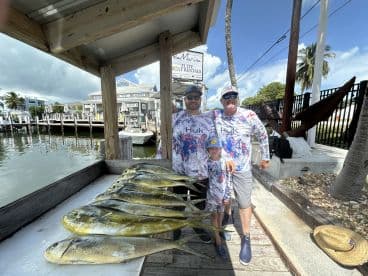 A family proudly displays their catch of Mahi Mahi on a catch board at a marina, showcasing a successful fishing trip.