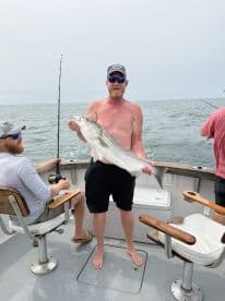 An angler proudly displaying a large Striped Bass while fishing on a charter boat, showcasing a successful day on the water.