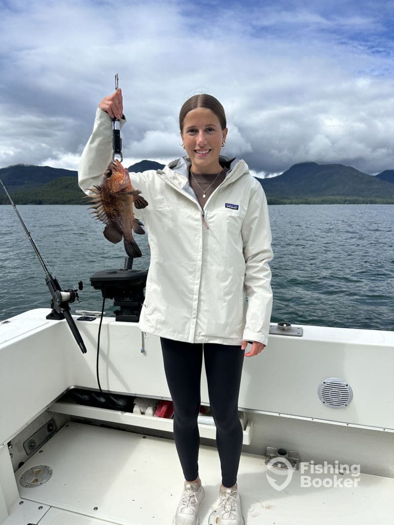 A young angler proudly displaying a freshly caught rockfish while aboard a fishing boat in a scenic coastal environment.
