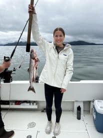 A young angler proudly displaying a freshly caught Salmon while fishing on a boat in a scenic coastal environment.