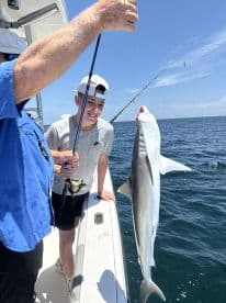 A young angler joyfully displaying a caught shark while fishing on a boat, enjoying a sunny day at sea.