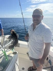 An angler proudly displaying a large Grouper while fishing on a boat in clear blue waters.