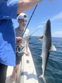 A young angler is excitedly holding a shark while fishing on a boat in open waters, showcasing a successful catch during a summer trip.