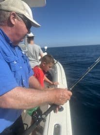 A young boy and an adult are engaged in fishing on a boat, with the boy focused on reeling in a catch while the adult assists, showcasing a family fishing experience.