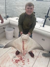 A young angler proudly displaying a large stingray on a fishing boat, showcasing the excitement of a successful catch.