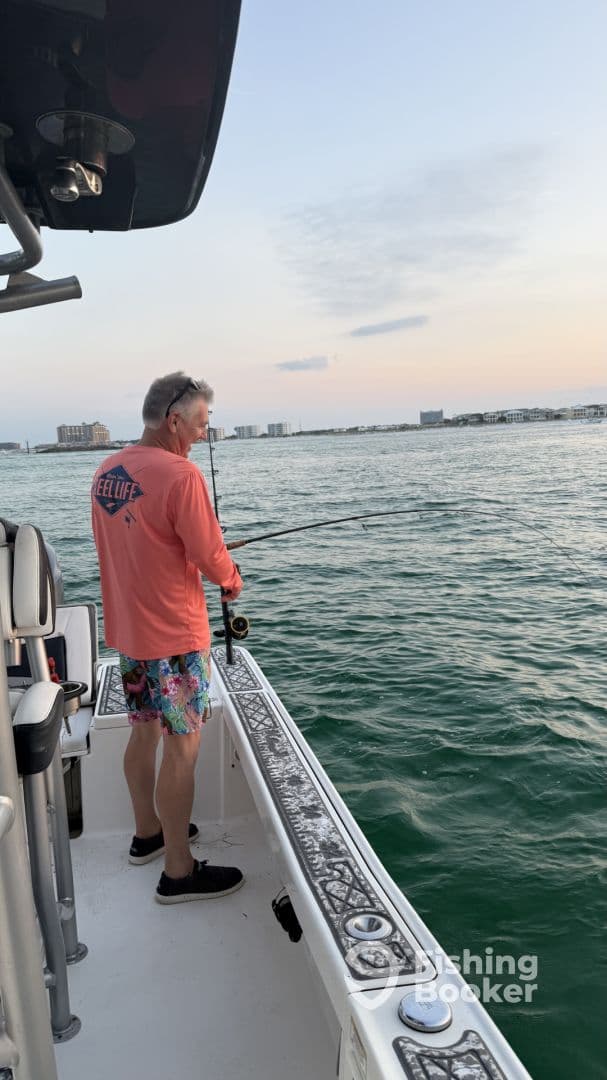 An angler casting a line from a boat during a serene evening fishing trip, with a coastal backdrop.