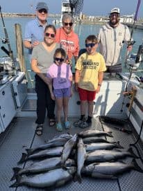 A family group proudly displaying their catch of multiple fish on a fishing charter, showcasing a successful day on the water.