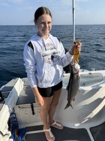 A young angler proudly displaying a caught Lake Trout while fishing on a boat in open water.