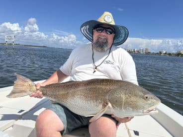 An angler proudly displaying a large Redfish while fishing in a scenic coastal environment.