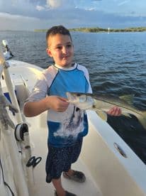 A young angler proudly displaying a Snook while fishing on a boat, enjoying a sunny day on the water.