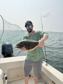 Angler displaying a large Flounder while fishing from a boat, showcasing a successful day on the water.
