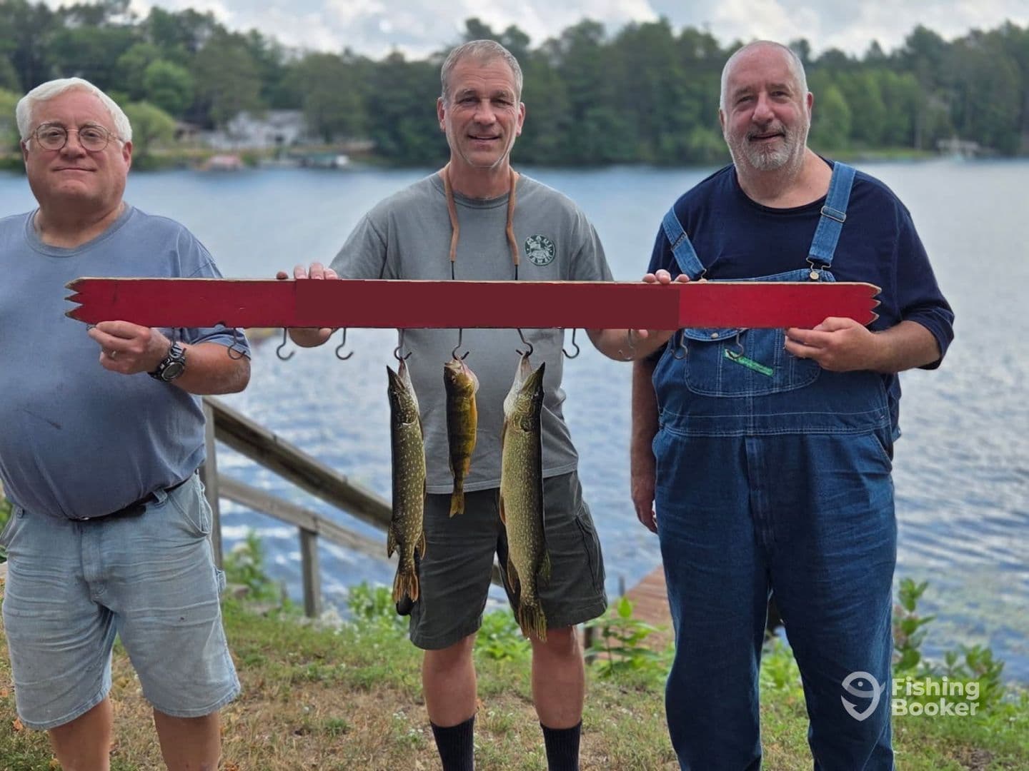 Three anglers proudly displaying their catch of Northern Pike on a catch board at a scenic lake, showcasing a successful fishing trip.