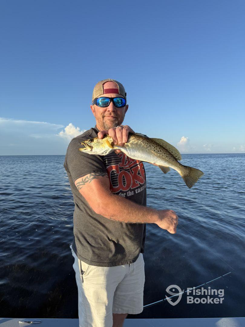 An angler proudly displaying a Speckled Trout while fishing on a calm day, showcasing the excitement of a successful catch.