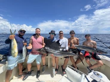 Group of anglers displaying their impressive catch, including a large Sailfish and other species, aboard a fishing boat in clear blue waters.