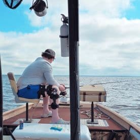 A solo angler fishing from a small boat, focused on the water while using a fishing rod, showcasing a serene day on the water.