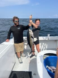 Two anglers proudly displaying a large Tuna on a fishing charter in open waters.