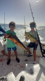Two young anglers proudly displaying their catch of Mahi Mahi while fishing on a boat, showcasing a fun day on the water.