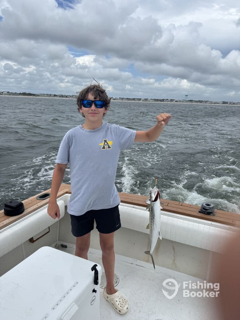 A young angler proudly displaying a caught fish while aboard a boat, with a scenic coastal backdrop.