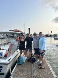 A group of five friends posing on the dock next to their fishing boat, ready for a day of fishing at the marina.