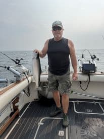 An angler proudly displaying a large Salmon on the deck of a fishing boat, showcasing a successful day on the water.