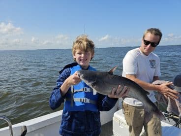 A young angler proudly holding a large catfish while fishing on a boat, showcasing a successful day on the water.