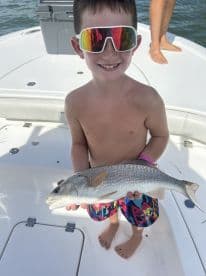 A young angler proudly displaying a caught Redfish while enjoying a sunny day on the boat.