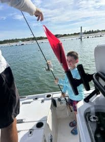 A young boy joyfully reeling in a fish while fishing from a boat, showcasing a fun day on the water.