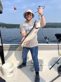 Angler proudly displaying a large Lake Trout while fishing on a serene lake, showcasing a beautiful summer day.