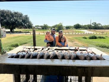 A family poses proudly behind a catch of multiple fish displayed on a cleaning table after a successful fishing trip.