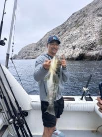 An angler proudly displaying a large Bass while fishing near rocky coastal waters.