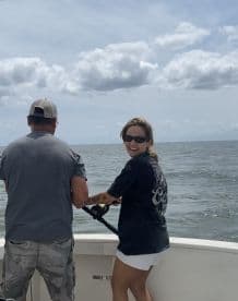 A woman and a man are actively fishing on a boat, with the woman smiling as she reels in a catch, showcasing a lively day on the water.