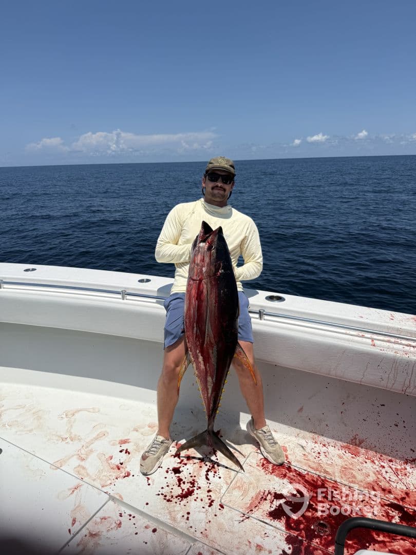 Angler proudly displaying a large Tuna on a fishing boat, showcasing a successful offshore fishing trip.