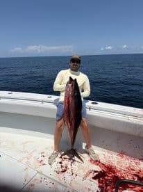 Angler proudly displaying a large Tuna on a fishing boat, showcasing a successful offshore fishing trip.