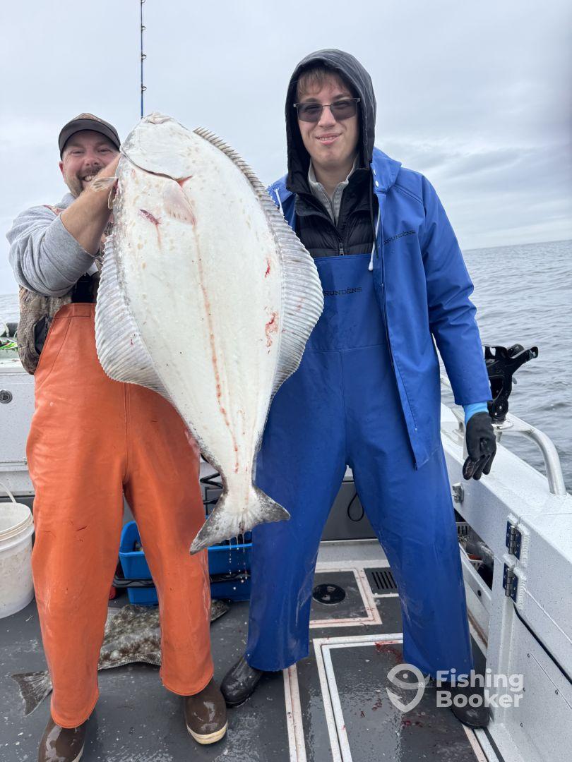 Two anglers proudly displaying a large Halibut on a fishing boat, showcasing a successful catch during a deep-sea fishing trip.