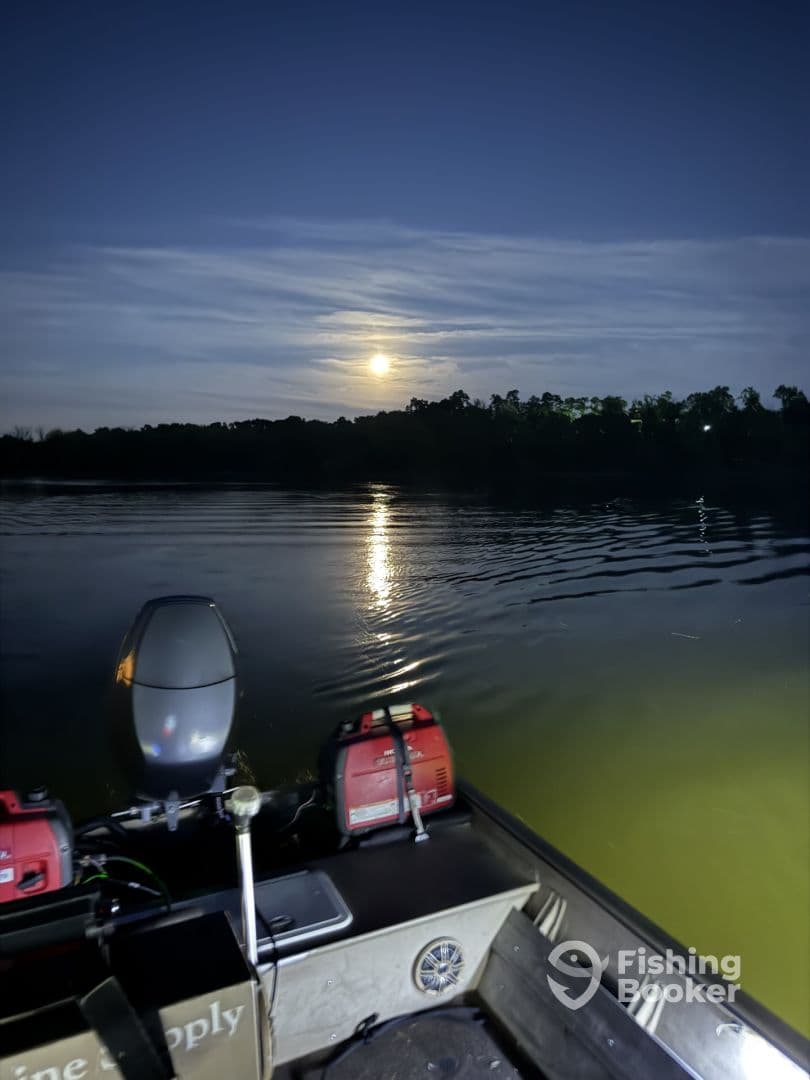A serene evening view from a small fishing boat on a calm lake, illuminated by the moonlight reflecting on the water.