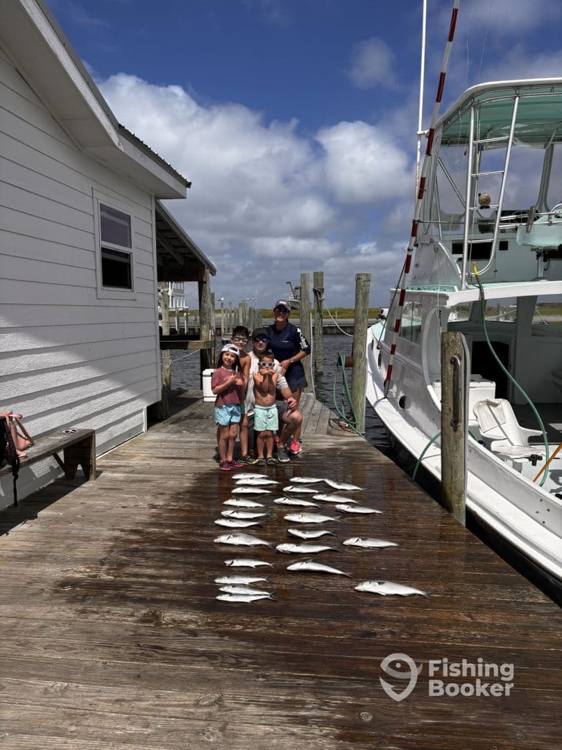 A group of young anglers proudly posing with their catch of the day, featuring a variety of fish laid out on the dock after a successful fishing trip.