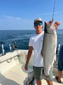A young angler proudly displaying a large fish on a fishing boat, with multiple fish visible on the deck, showcasing a successful day on the water.