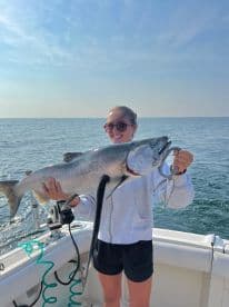 An angler proudly displaying a large Salmon while fishing on a boat in open waters.