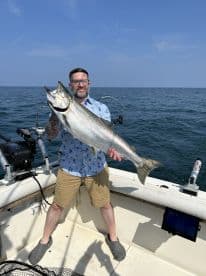 An angler proudly displaying a large Salmon while fishing offshore, showcasing a successful day on the water.