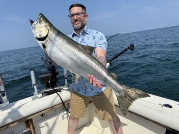 An angler proudly displaying a large Lake Trout while fishing on a boat in open water.